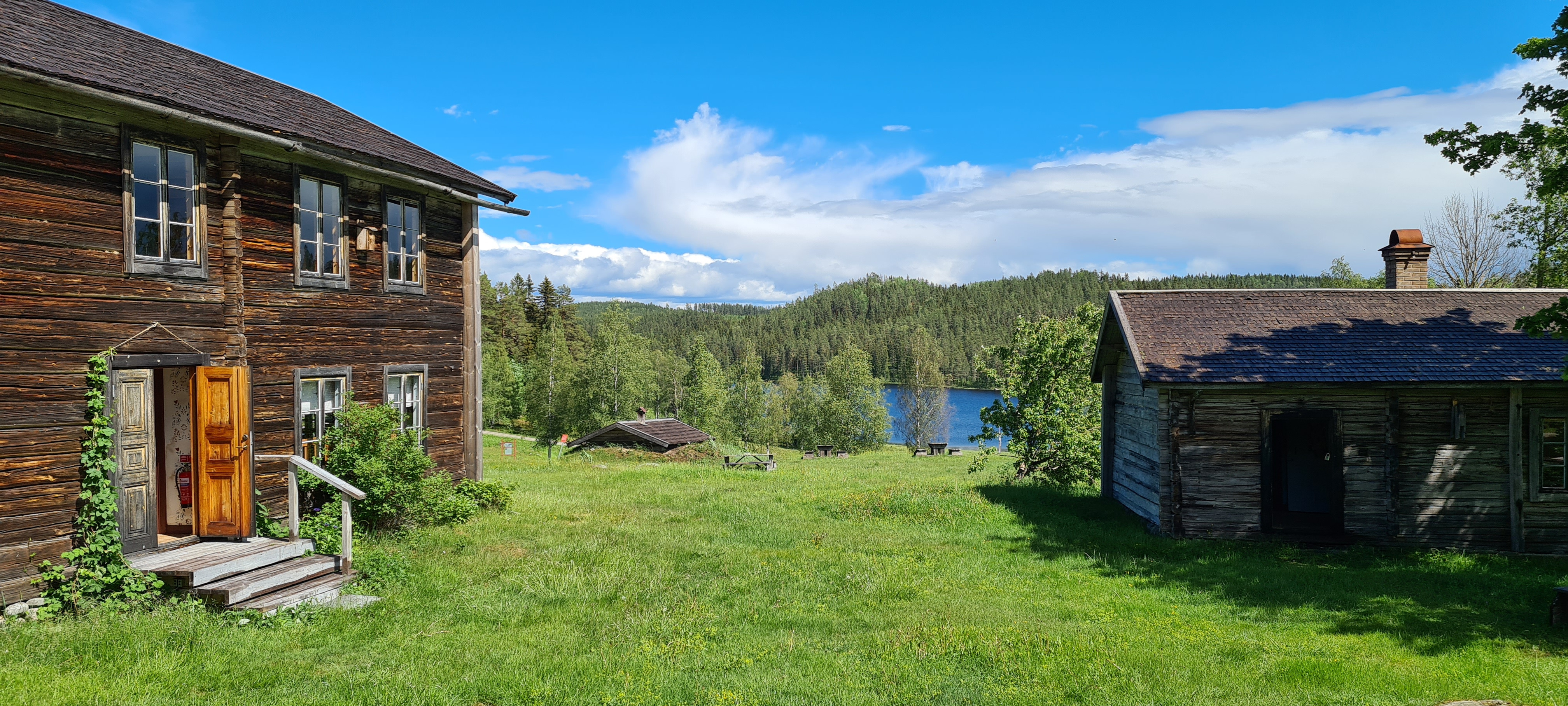 Två gamla timmerhus och utsikt ner mot en tjärn. Foto: Sundsvalls kommun.