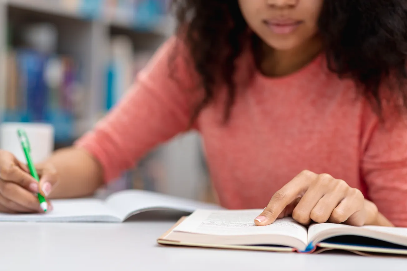 En kvinna sitter vid ett bord med en bok och en penna.