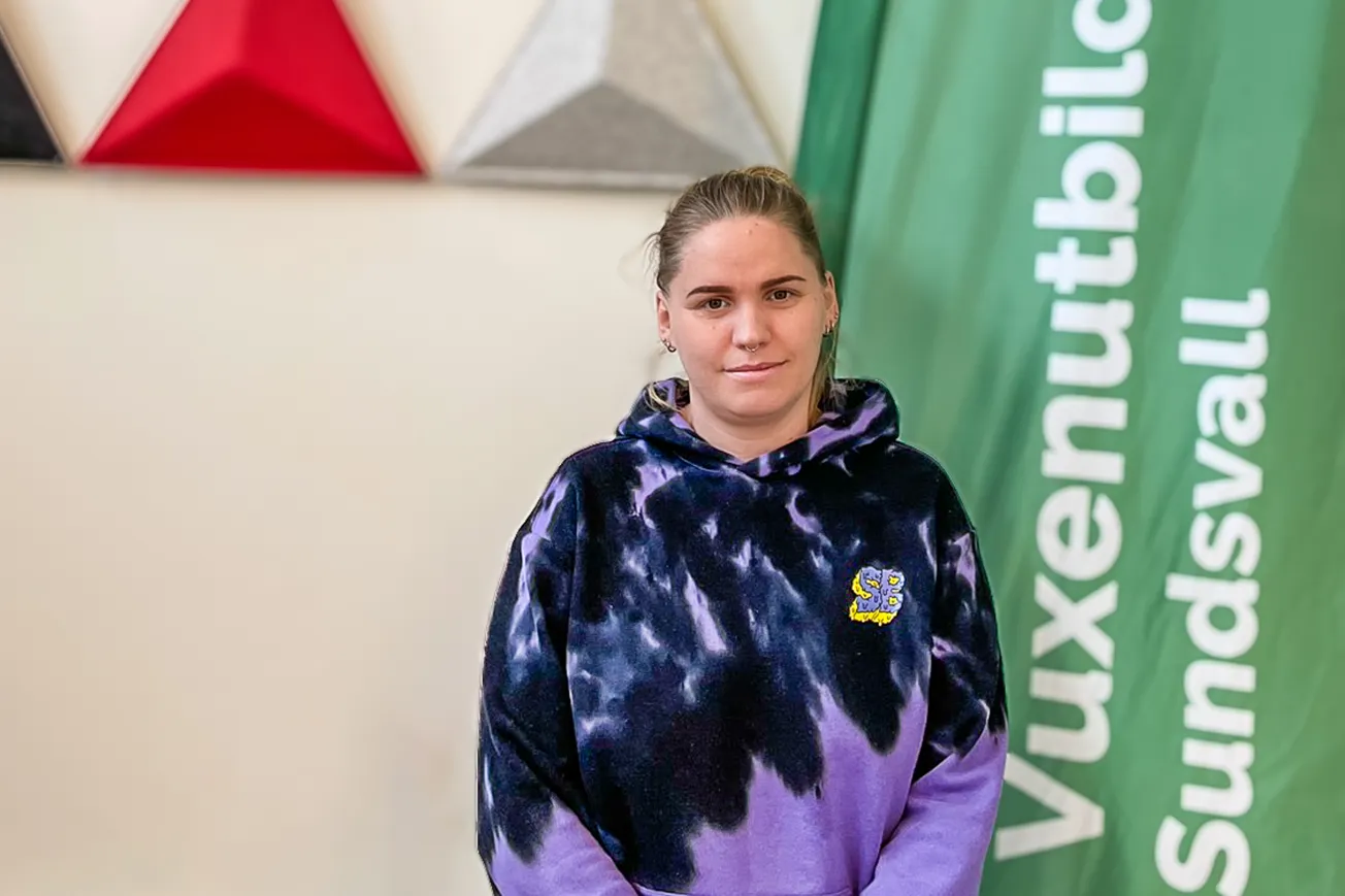 En elev står framför en grön och vit banderoll som det står Vuxenutbildning Sundsvall på