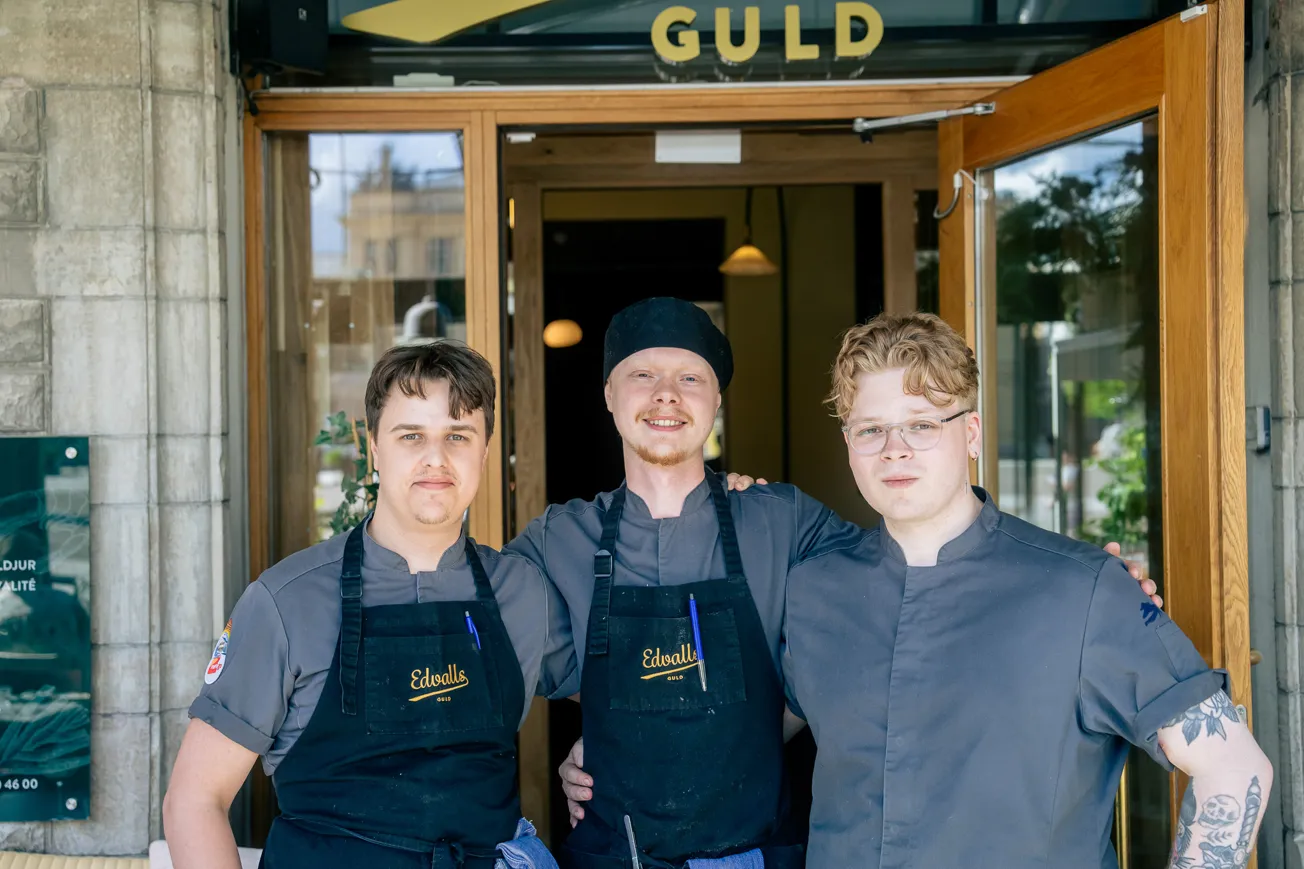 Tre män som står bredvid varandra framför restaurangen de jobbar på.