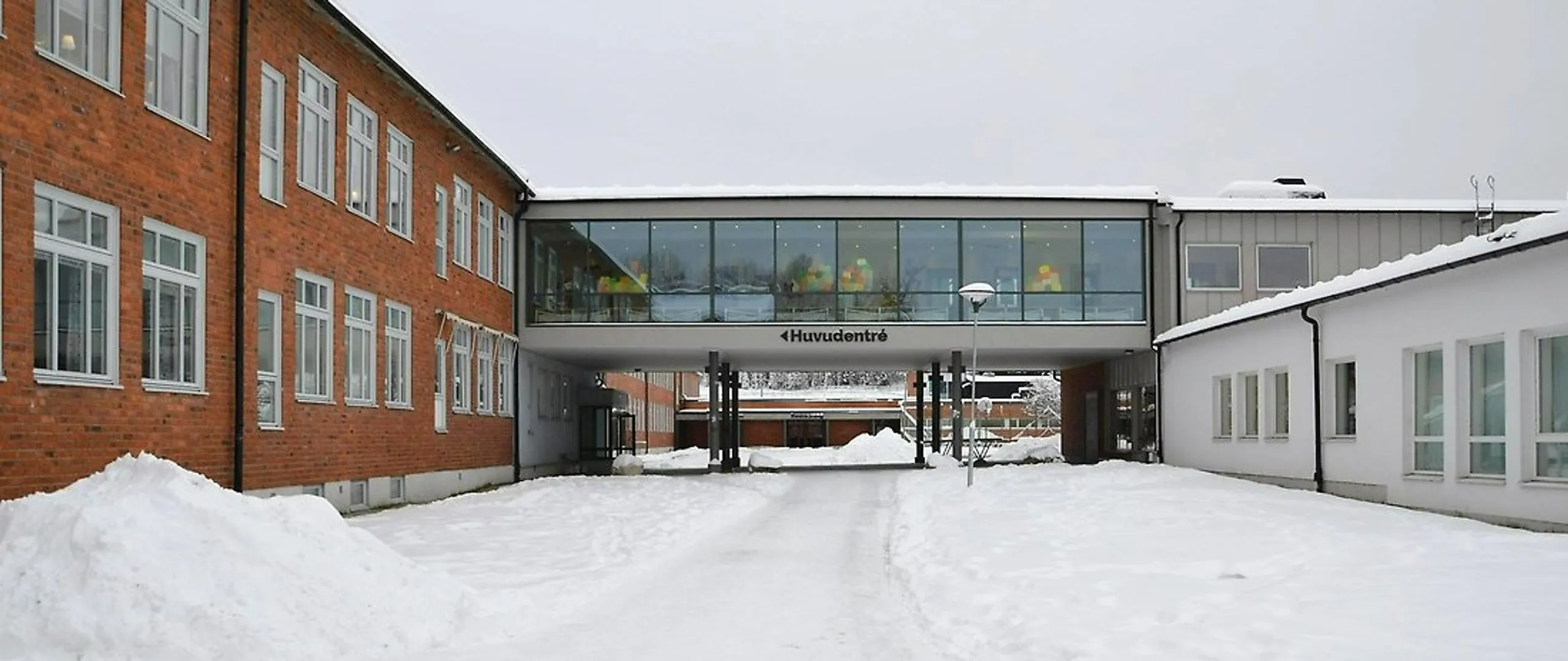 En snötäckt gata med en skolbyggnad i tegel i bakgrunden.