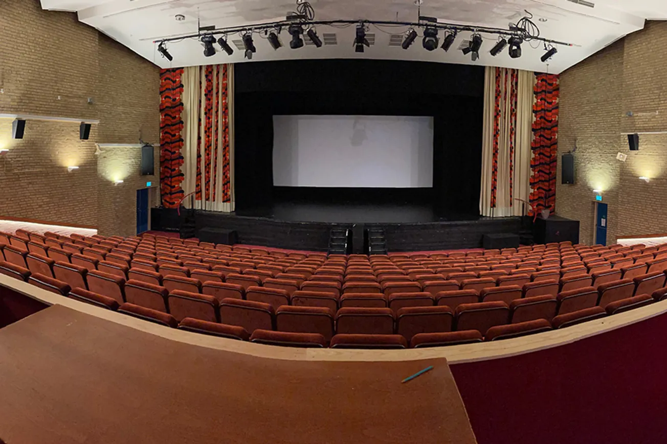 Ett tomt auditorium med en projektorduk och röda stolar.