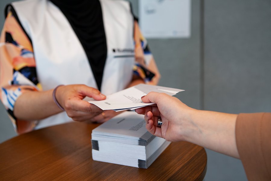 Hand som lämnar över valkuvert till person med vit väst.