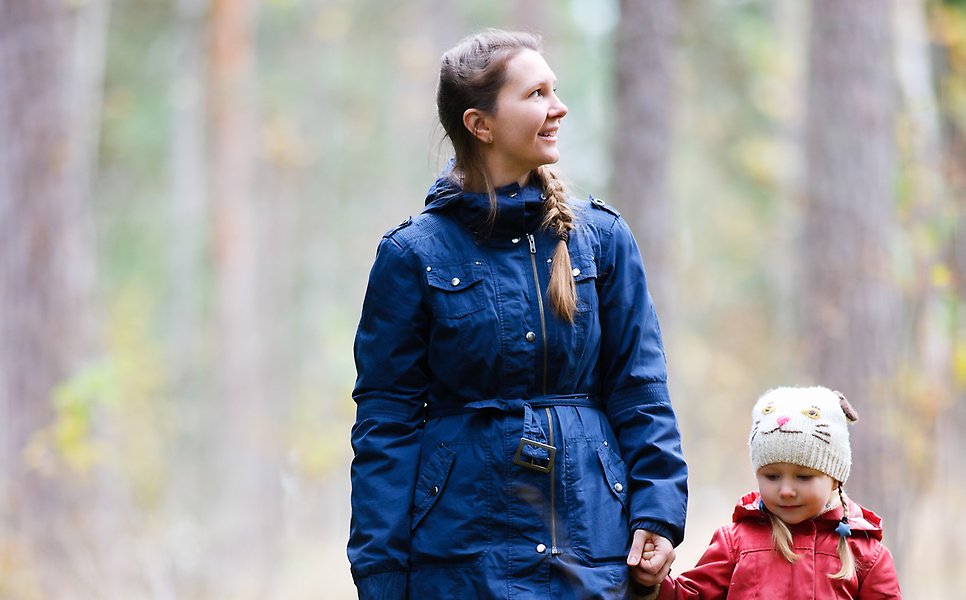 En vuxen och ett barn går hand i hand och tittar sig runt i skogen. 