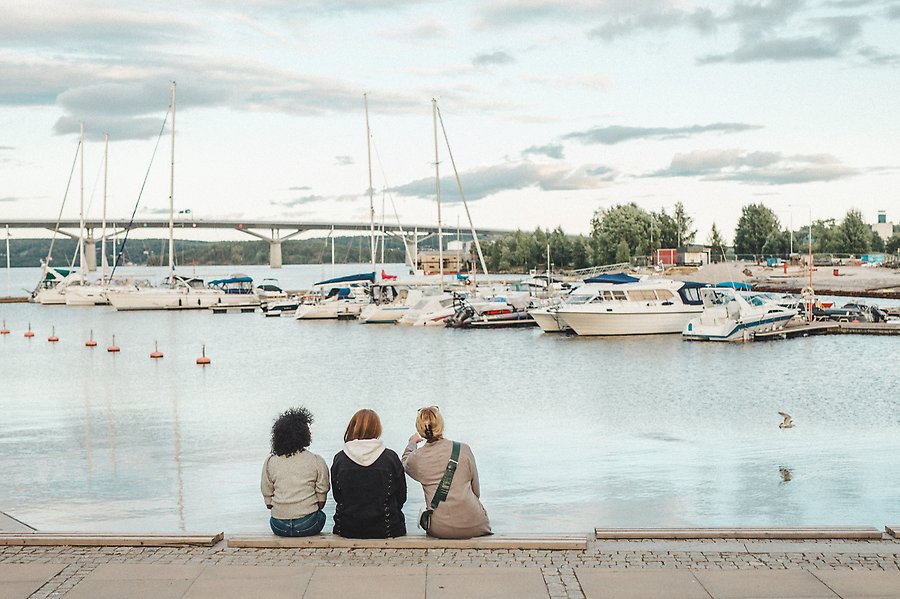 Tre kvinnor sitter vid småbåtshamnen i Sundsvall. Alla tre spanar ut mot havet och många båtar ligger fasttöjda på rad.